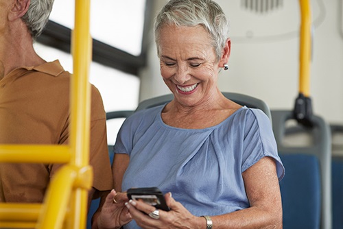 Patiente atteinte  d'ostéoporose - Sarah dans un bus écrit sur son smartphone en souriant